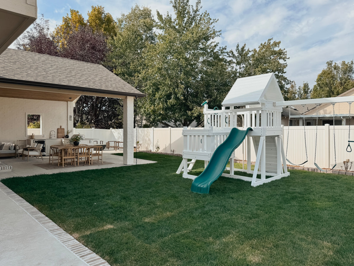 White Congo playset with a green slide in a landscaped backyard